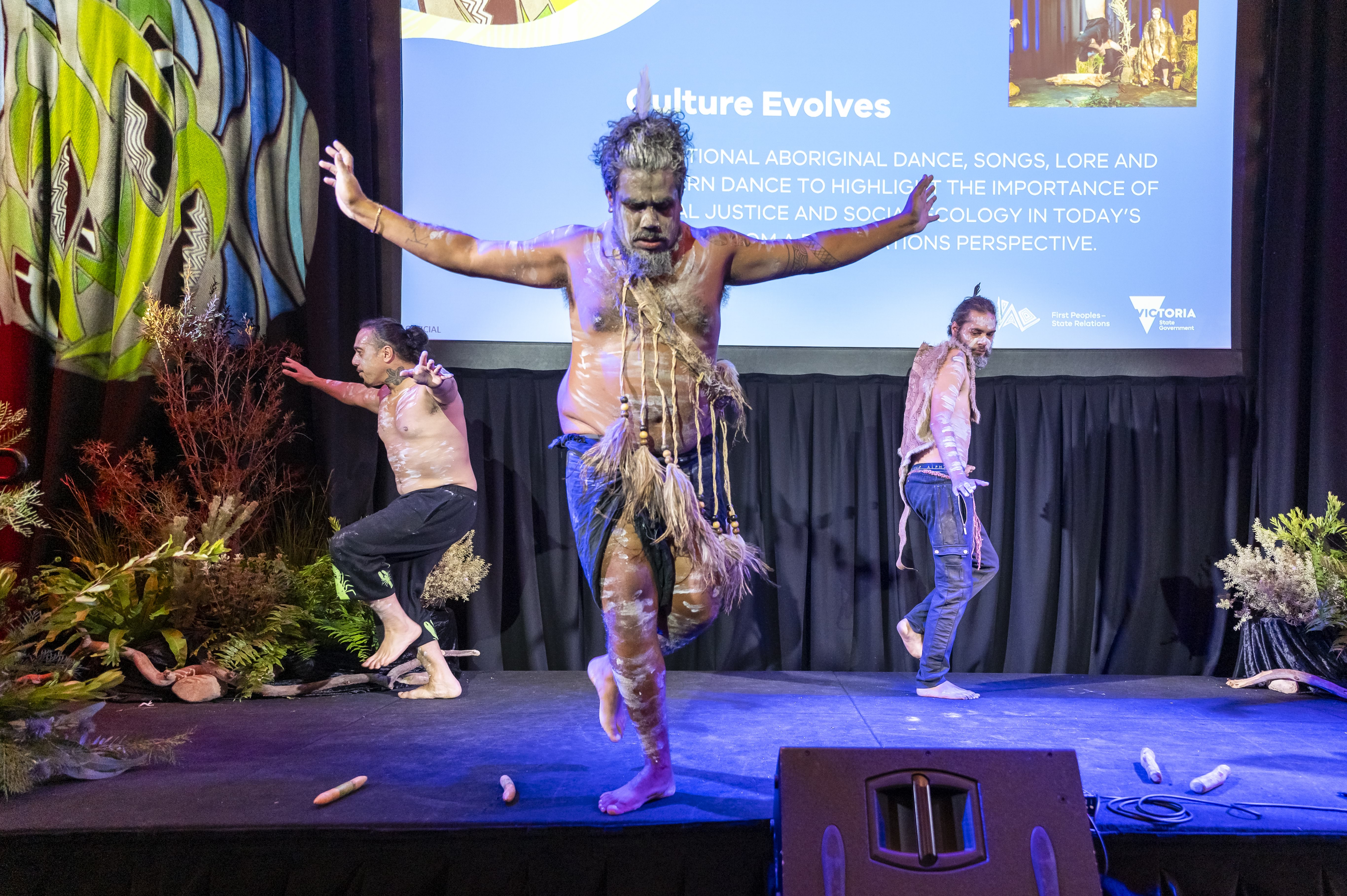 Three men perform a traditional Aboriginal dance on stage.